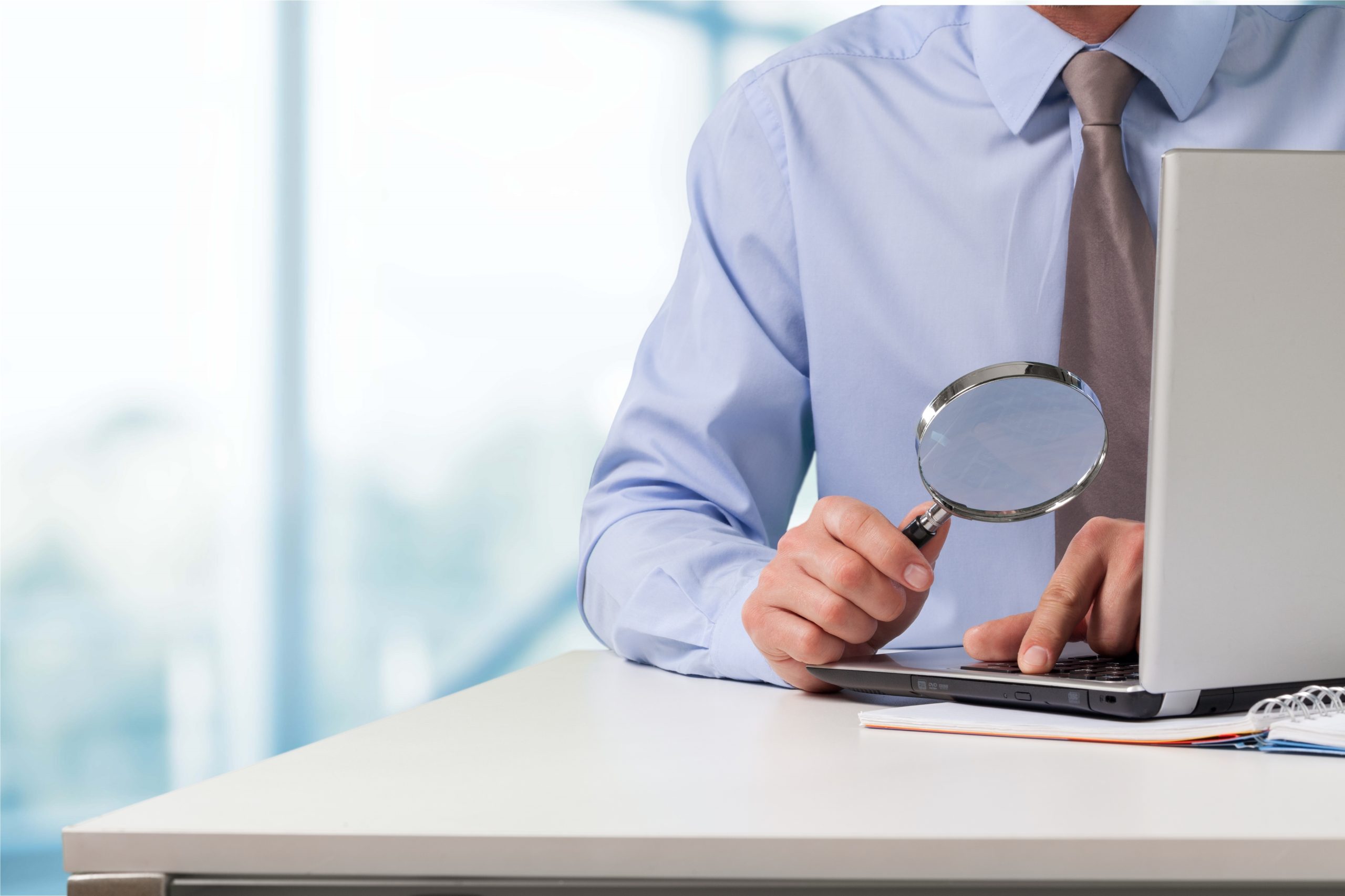Businessman looking at his laptop through magnifying glass